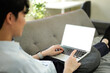 © Stella 16 - Young male tech user relaxing on sofa holding laptop computer mock up blank white screen.