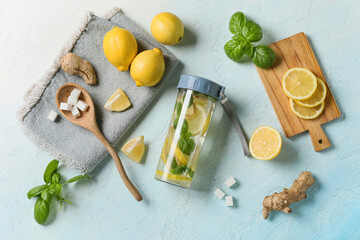 Wall Mural - Bottle of infused water with basil leaves, ginger, lemons and sugar cubes on light blue background