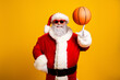 © deagreez - Santa Claus spinning a basketball on his finger, wearing sunglass and a festive outfit, standing against a bright yellow background