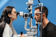 © wedmoments.stock - Female ophthalmologist conducting a vision examination using a slit lamp on a male patient with blue background, showcasing the importance of eye health and professional care