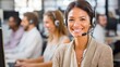© mila103 - A friendly customer service representative smiles as she answers calls at a lively call center. Team members are engaged in assisting clients showcasing a collaborative work environment.