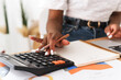 © etonastenka - Close-up shot of an African American womans hand pressing calculator buttons while counting bills and managing finances at home. Concept of accounting, personal budget, or financial planning for