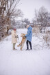 © StockMediaSeller - Two people with a Golden Retriever enjoying a snowy walk in a rural winter landscape. The large dog stands on its hind legs greeting one person while the other holds the leash.