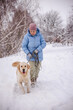 © StockMediaSeller - Elderly woman walking her cheerful Golden Retriever on a snowy rural path. The dog joyfully trots ahead while the woman holds the leash, enjoying a calm winter walk among snow-covered trees.