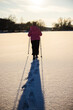 © StockMediaSeller - Woman walking with trekking poles on a snow-covered frozen lake during sunset. Her long shadow stretches across the glistening snow, symbolizing solitude, strength, and peaceful winter activity.
