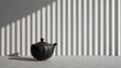 © Nitchalee N. - Korean tea ritual, A black pot sits on a surface, casting shadows from striped light against a textured wall, creating a striking visual contrast.