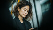 © Art of Ngu - Young woman with wavy hair using smartphone on subway, thoughtful commuter in black jacket during urban transit with soft natural light