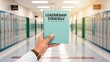 © Tonton1541 - leadership education sector concept. Hand holding a book titled 'Leadership Strategy' in a school hallway.