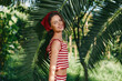 © SHOTPRIME STUDIO - A cheerful woman poses in a sunny tropical garden wearing a red striped top and head scarf. She smiles warmly, creating a lively outdoor moment filled with light and vitality.