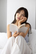 © hidez - Young Woman Reading a Book in Bed with Bright Natural Morning Light
