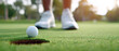 © praewpailyn - Golf ball near hole on green grass with blurred golf shoes in background during sunny day for golf sport enjoyment