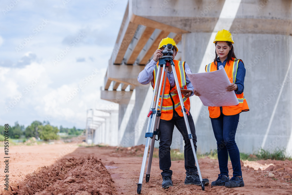 Two civil engineers wearing helmets and reflective vests survey a ...