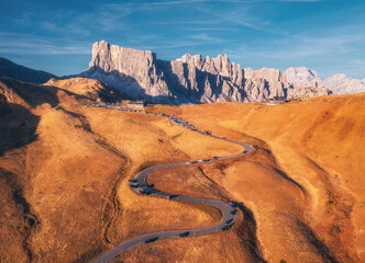 Wall Mural - Aerial view of winding road in mountain pass at sunset in autumn. Passo Giau, Dolomites, Italy. Beautiful roadway, orange grass, cars, alpine meadows, sky with clouds. Landscape with highway in fall