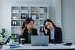 © MINAE - Two businesswomen discussing work problems in an office, one expressing frustration and headache while the other explains, highlighting workplace stress and disagreement