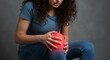 © jen - Woman clutches her knee, which is highlighted in red, against a blurred gray backdrop