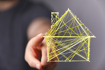 Wall Mural - Abstract illustration of a hand pointing at a 3D house made of yellow lines. Represents real estate, future, technology, and digital home concep