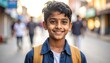© barabiri - A smiling boy with a backpack and a red dot on his forehead stands on a street, blurred background with people