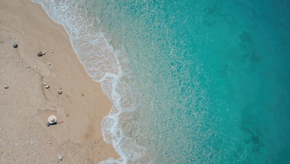  Bird's-eye perspective of a woman reclining on a sandy shore beside crystal-clear ocean waves under bright summer skies