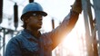 © Thares2020 - A focused electrical engineer in a hard hat and safety glasses stands in a power substation at sunrise with warm sunlight and flare