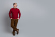 © deagreez - Handsome mature businessman in casual red sweater and glasses standing with crossed legs against plain background