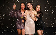 © Prostock-studio - Cheerful attractive diverse ladies in nice outfits posing together among falling confetti over black background, holding photo booth pops, grimacing and gesturing. New Year party