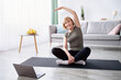 © Prostock-studio - Flexibility exercises for healthier living. Athletic senior woman doing yoga in front of laptop during home workout. Attractive mature lady practicing pilates, leading sporty lifestyle, copy space