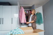 © okrasiuk - Middle aged woman selecting clothes from wardrobe for donating to Charity shop. Decluttering, Sorting clothes and Cleaning Up. Reuse, second-hand concept. Conscious consumer, sustainable lifestyle.