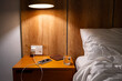 © zhennyzhenny - Mobile phone charging on bedside table in comfortable hotel or home bedroom.