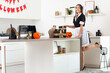 © Pixel-Shot - Young happy woman dressed as dead maid for Halloween with gift boxes, human skull and pumpkins on table in kitchen