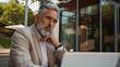 © Mutshino_Artwork - Confident mature businessman using laptop outside contemporary office building