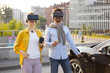 © sofiko14 - A couple wearing VR headsets waits while their electric vehicle charges in an urban setting.