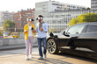 © sofiko14 - A couple wearing VR headsets walks near a charging electric vehicle in an urban setting.