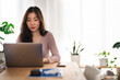 © Studio Marmellata - A young woman works on her laptop at a wooden desk, surrounded by plants and natural light.
