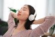 © Studio Marmellata - A young woman with her eyes closed enjoys music through her headphones, resting her head back with her hands behind her neck.