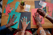 © Seventyfour - Black man, Black woman, and Black child creating Kwanzaa crafts by tracing and cutting hand shapes from colored paper, arranging materials on wooden table, celebrating cultural tradition together