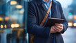 © Kateryna - torso with a crossbody strap and tablet peeking from a sleeve street reflections on glass defocused crisp edge light empty space left urban professional mob