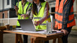 © saltdium - Close-up of engineers planning construction with a laptop and architectural model on a worktable at a building site