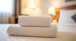 © Hena - Two white towels are stacked on a bed in a hotel room