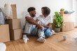 © lordn - African American couple sitting on the floor of their new apartment surrounded by moving boxes, smiling and talking together, enjoying a peaceful break while unpacking and settling into their home