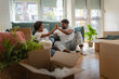 © lordn - Happy African American couple sitting on the floor surrounded by boxes in their new home, giving each other a high five and celebrating a successful moving day