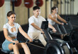© JackF - Workout girl cross training exercising cardio using rowing machine with group of people in crossfit club