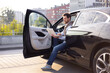 © sofiko14 - A man sits in a black car, working on a laptop with the door open, likely in a city setting.
