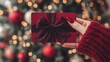 © Rifqi - Female hand in red sweater holds red gift card with bow in front of blurred Christmas tree, concept for holiday promotions, seasonal discounts and festive gift-giving occasions