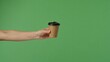 © kinomaster - A woman hand extends into the frame, holding a brown paper coffee cup with a black lid, against a green background.