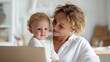 © iuricazac - A mother holding a baby while using a laptop at home.
