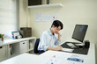 © Stella 16 - Young man reading documents at desk in modern office with computer and bookshelf nearby, showcasing a professional work environment under soft natural light.