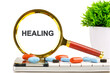 © Garik - A magnifying glass highlights the word healing among various pills and supplements, with a touch of greenery symbolizing natures role in health and wellness