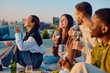 © we.bond.creations - Group of diverse friends relaxing and laughing together, drinking wine and eating snacks on a rooftop at sunset