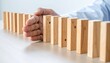 © Haven - A hand stopping a falling line of wooden domino blocks on a table, symbolizing intervention and prevention.