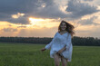 © shymar27 - Female figure in white dress runs through green field at sunset, surrounded by nature's beauty, evoking feelings of joy and freedom in a serene environment